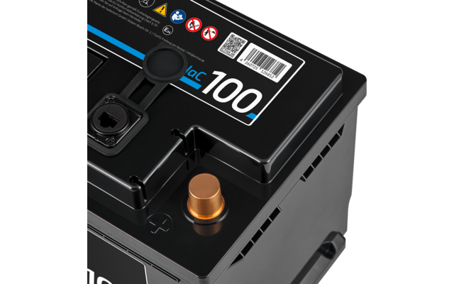 Nahaufnahme der oberen Ecke einer schwarzen Batterie mit kupferfarbenem Pluspol und eingeformtem Pluszeichen, Aufkleber mit der Zahl 100, QR-Code, Warnsymbole und Kunststoffgriff