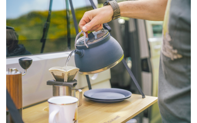 Hand giet hete thee uit een ketel in een kopje op een buitentafel