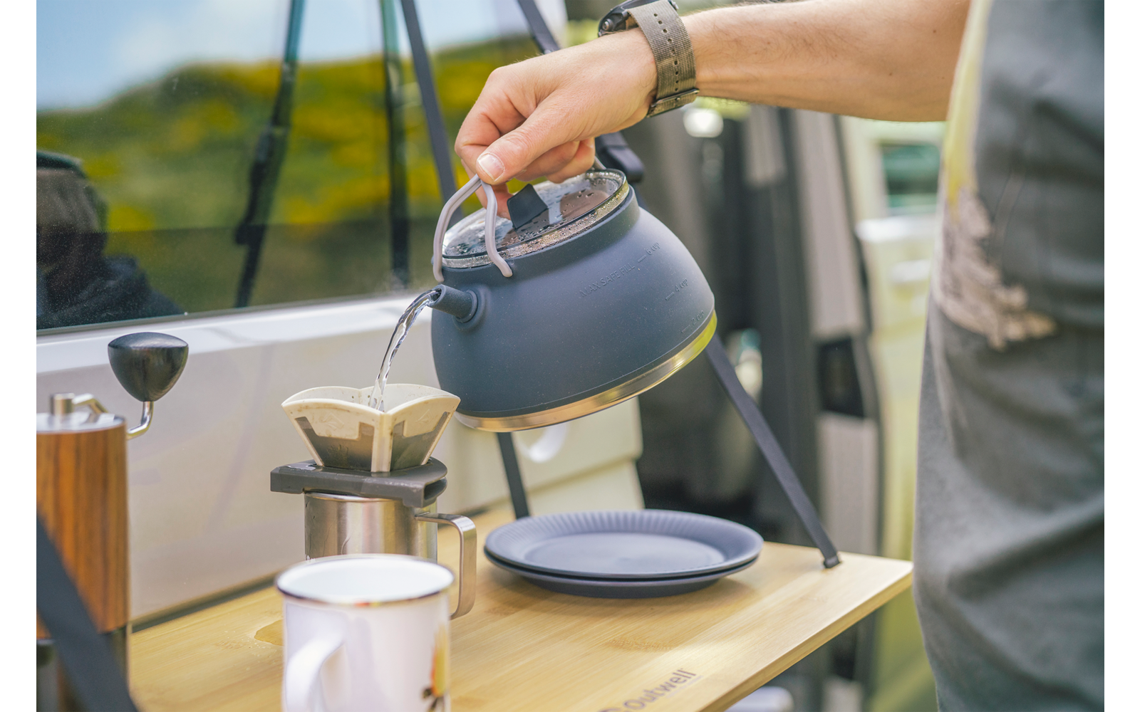 Hand giet hete thee uit een ketel in een kopje op een buitentafel