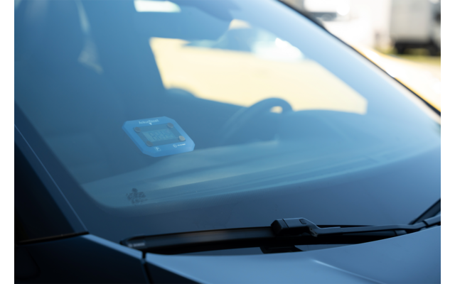 Pare-brise d'une voiture avec essuie-glace, un petit appareil bleu sur le tableau de bord à l'intérieur et le volant en arrière-plan