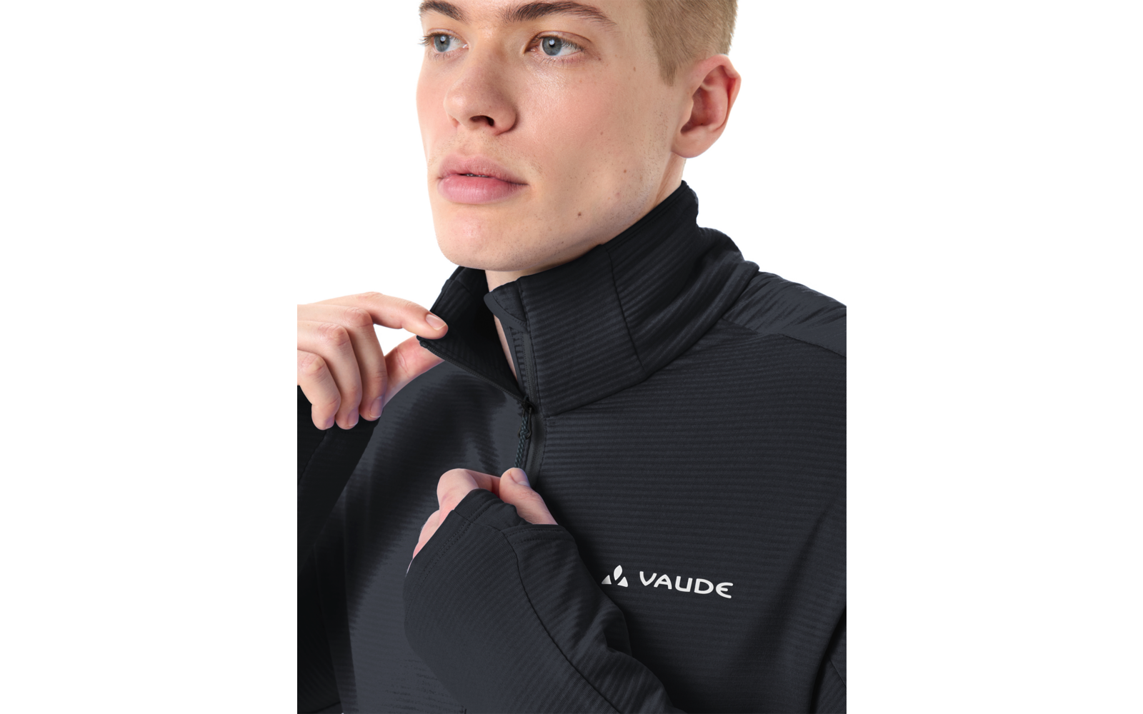 Person mit kurzem blondem Haar zieht den Reißverschluss am Kragen einer schwarzen VAUDE-Jacke hoch; Daumenloch in der Ärmelmanschette sichtbar