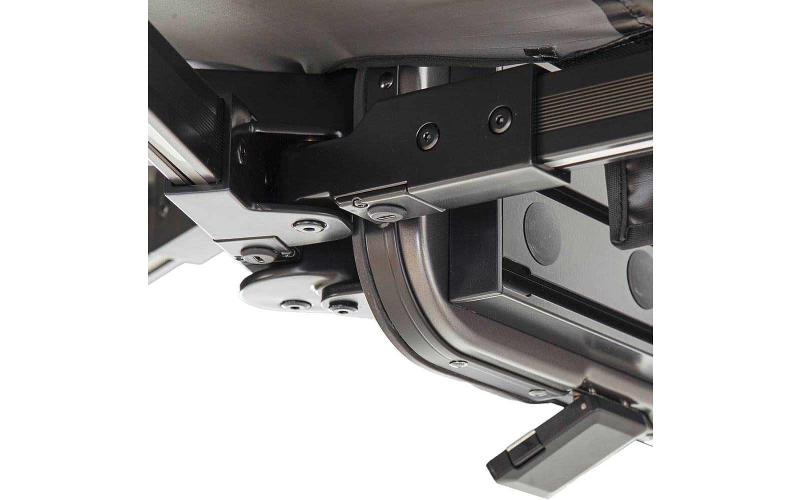 Nahaufnahme einer schwarzen Rad- und Scharniermechanik mit Schrauben, Metallplatten und grauem Stoff im Hintergrund