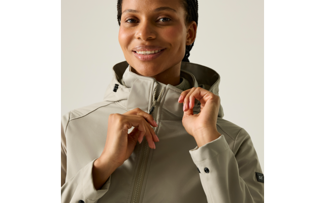 Nahaufnahme einer lächelnden Person mit geflochtenen Haaren, die den Reißverschluss einer hellgrauen Kapuzenjacke hochzieht