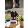Black portable lantern on a wooden table, next to a small pot with green leaves, blurred background