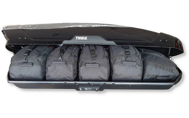 Coffre de toit Thule noir ouvert contenant quatre sacs de voyage noirs alignés côte à côte