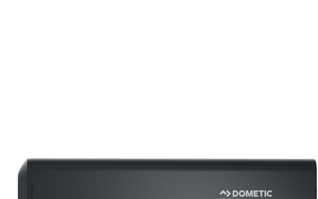 Dunkelgraues rechteckiges Gehäuse mit Dometic-Logo oben, zwei Anschlussklemmen links (rot und schwarz) und zwei Klappen an der unteren Vorderseite