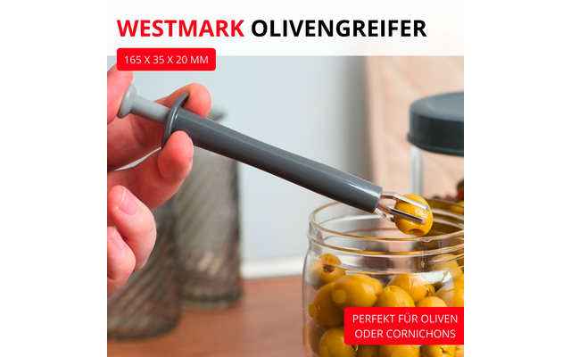 Main tenant un attrape-olive gris retirant une olive verte d'un bocal en verre rempli d'olives sur une surface en bois