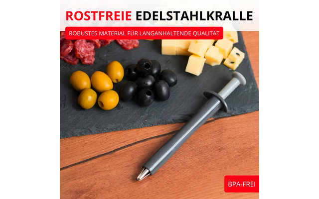 Outil métallique gris avec piston sur table en bois à côté d'une ardoise contenant des olives vertes et noires, des cubes de fromage et des tranches de salami ; texte rouge ROSTFREIE EDELSTAHLKRALLE et label rouge BPA-FREI