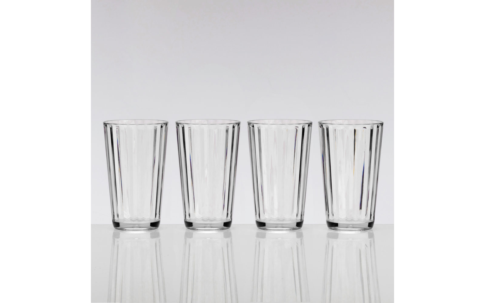 Quatre verres transparents côte à côte sur une surface blanche réfléchissante devant un fond gris clair