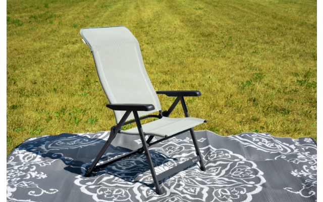 Weiß bespannter Stuhl mit schwarzem Gestell auf einer grauen, ornamentalen Decke auf grünem Gras