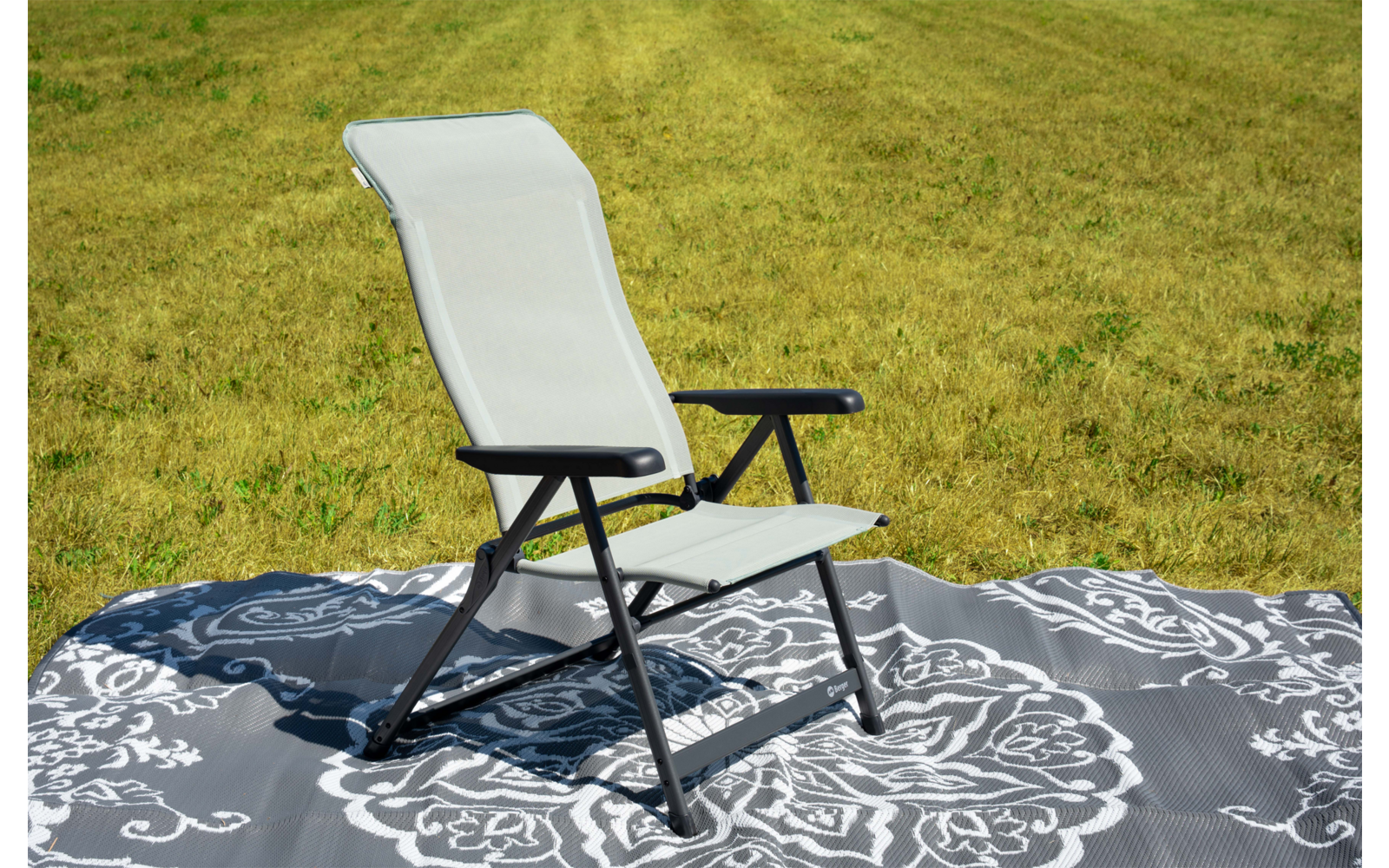 Weiß bespannter Stuhl mit schwarzem Gestell auf einer grauen, ornamentalen Decke auf grünem Gras