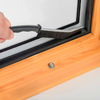 Mano sosteniendo un cepillo pequeño junto al borde interior de una ventana de doble acristalamiento con marco de madera; sujeción metálica en el alféizar