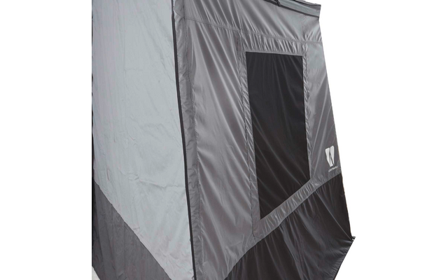 Nahaufnahme einer grauen und schwarzen Stofffläche mit einem dunklen rechteckigen Fenster, sichtbaren Nähten und einem weißen Logo unten rechts