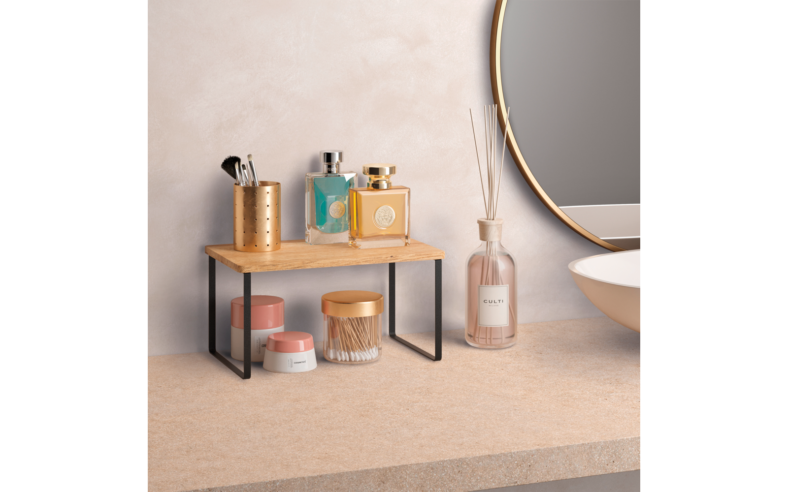 Kleine Holzablage mit schwarzen Metallfüßen auf einer Arbeitsfläche; auf der Ablage ein Metallbecher mit Make-up-Pinseln und zwei rechteckige Glasflaschen; unter der Ablage drei kleine Cremedöschen; rechts eine Glasflasche mit dünnen Stäbchen; Rand e
