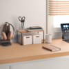 Schreibtisch mit Kopfhörern auf einem Ständer, kleinem Holzregal mit zwei weißen Aufbewahrungsboxen und Stapel Notizbücher, Stiftebehälter mit Schere und Stiften, Kaffeetasse, geschlossenes Notizbuch, Tablet mit Display und Fenster mit Jalousien
