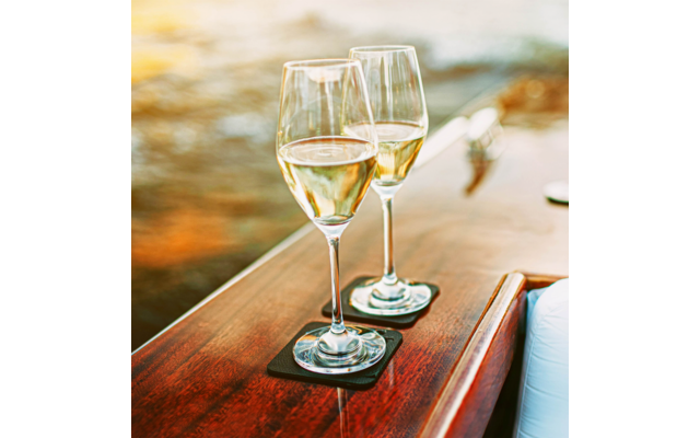 Zwei Weingläser mit weißem Wein stehen auf einem Holzgeländer mit Wasser im Hintergrund