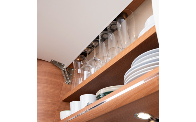 Open wooden kitchen cabinet with upside-down wine glasses on a rack, stacked plates, mugs and bowls