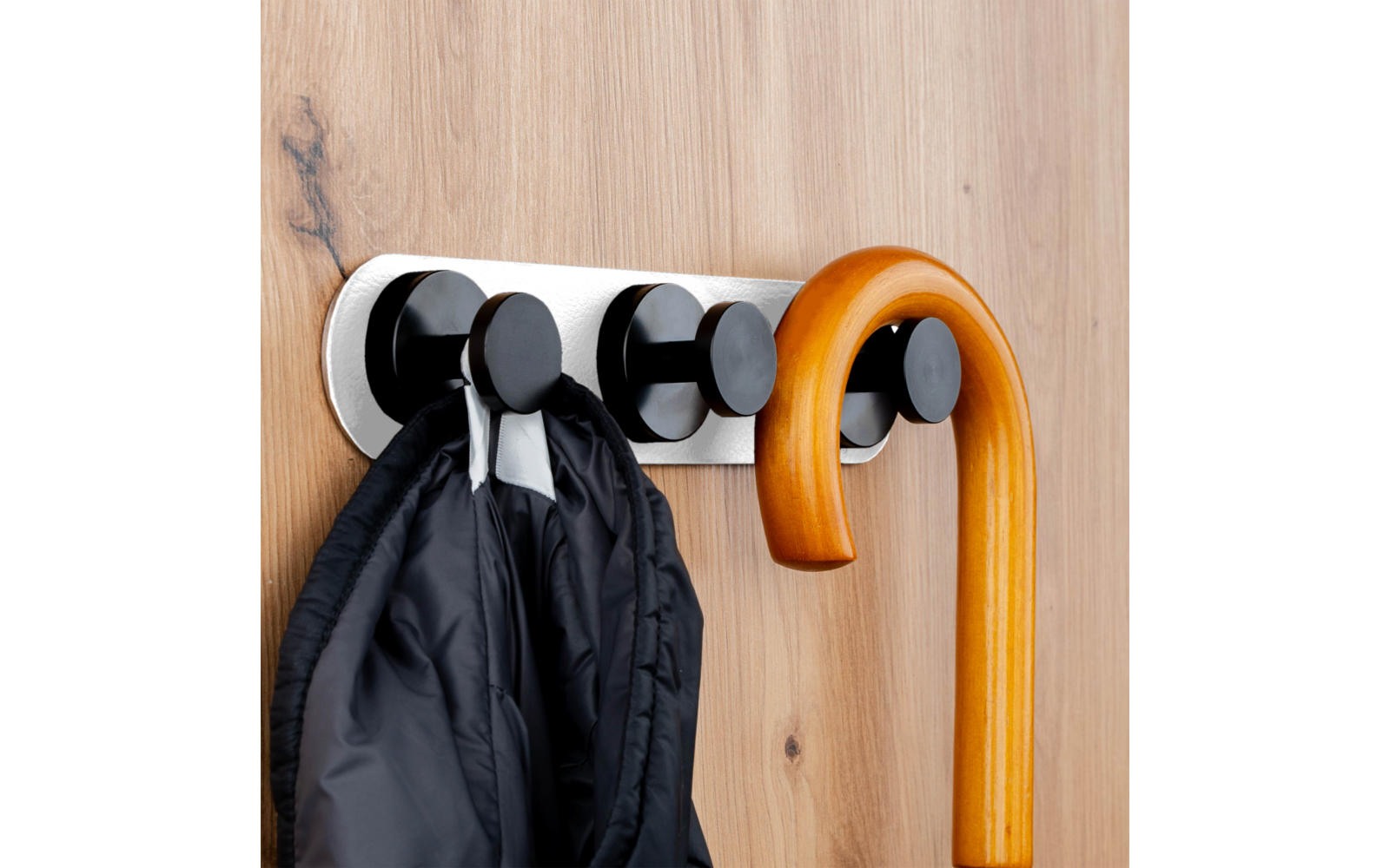 Black coat and light brown walking cane hanging on black hooks on a wooden rail
