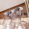 Several upside-down clear glass drinking glasses hanging under a wooden beam