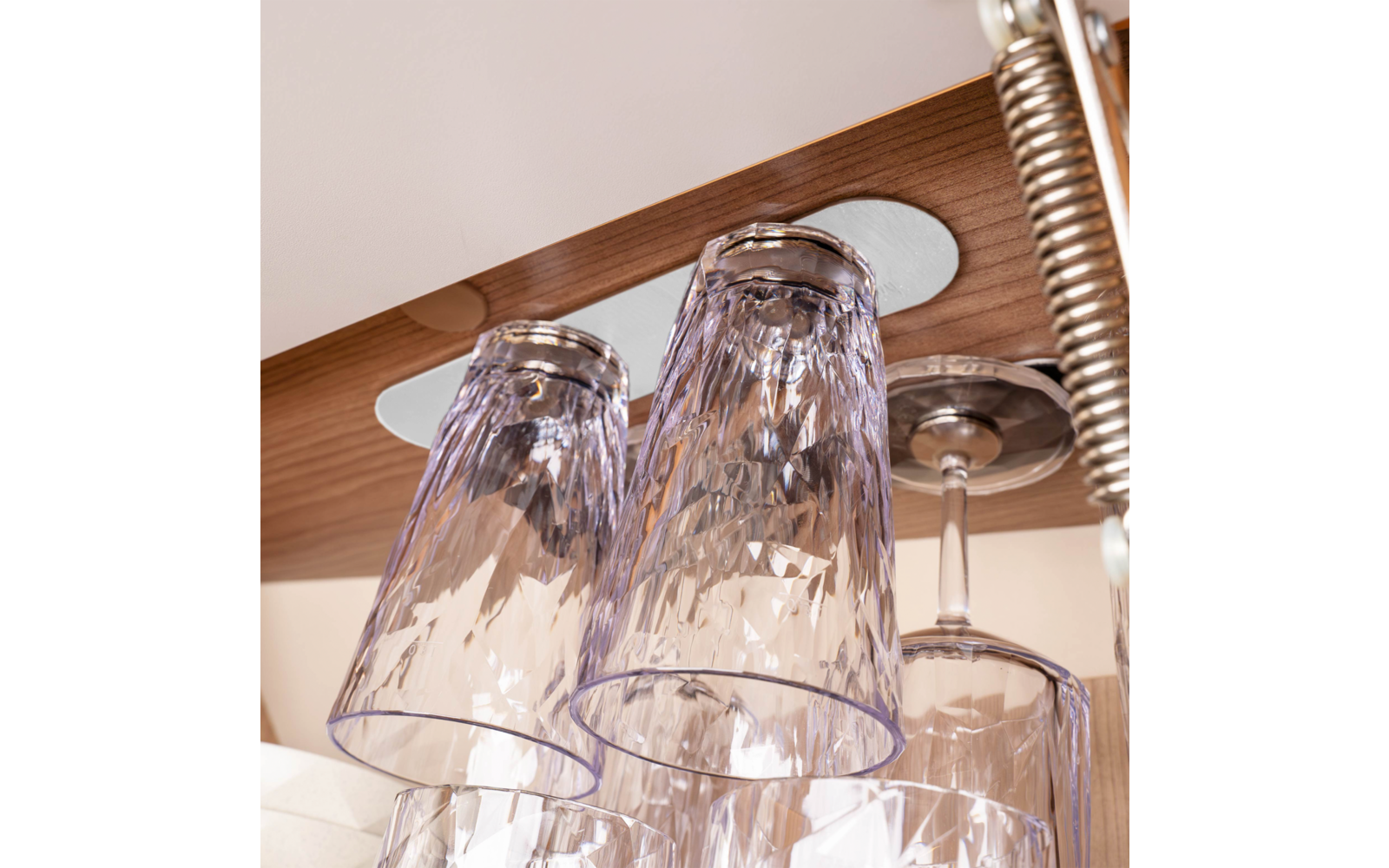Several upside-down clear glass drinking glasses hanging under a wooden beam