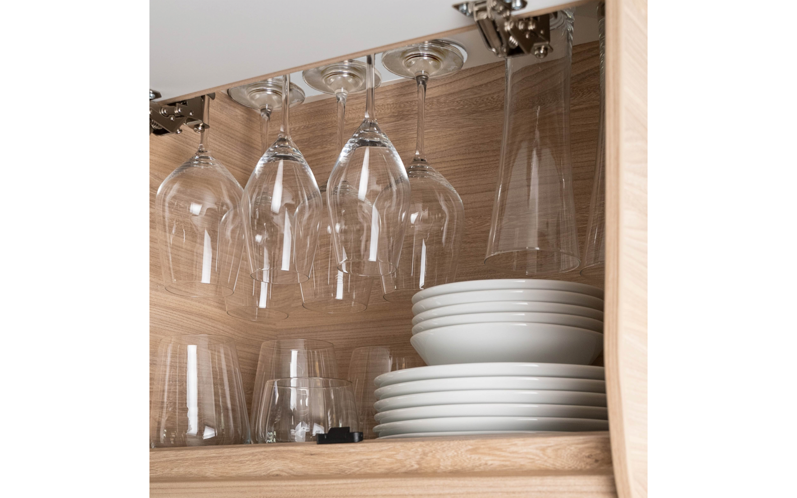 Wine glasses hanging upside down in a wooden cabinet, stacked white plates and additional glasses below