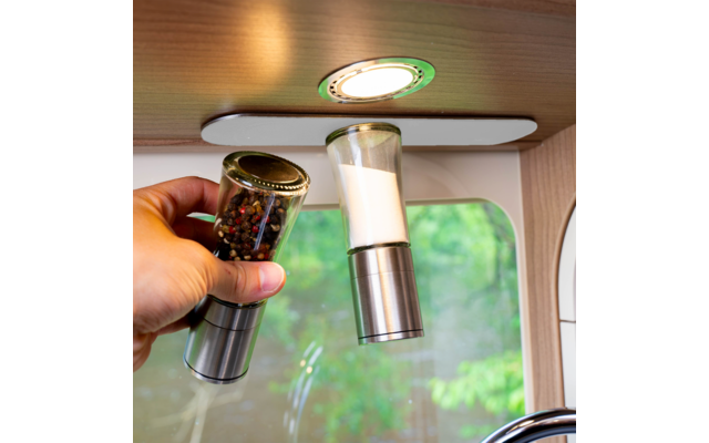 Hand holding pepper grinder next to a salt grinder under a kitchen light
