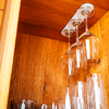 Three hanging wine glasses and several glasses rest inside a wooden cabinet