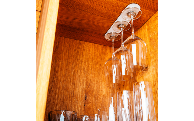 Three hanging wine glasses and several glasses rest inside a wooden cabinet
