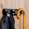 Black wall-mounted coat rack with round hooks on light wood, holding a black jacket and a curved wooden cane