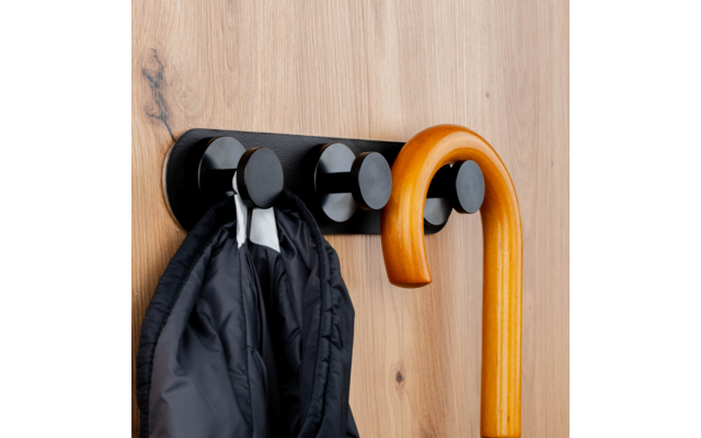 Black wall-mounted coat rack with round hooks on light wood, holding a black jacket and a curved wooden cane
