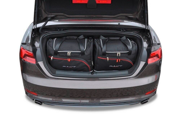 Geöffneter Kofferraum eines grauen Autos mit zwei schwarzen Reisetaschen mit roten Details nebeneinander