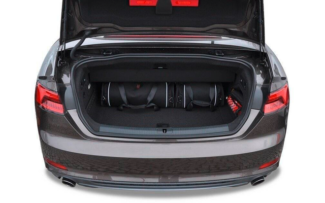 Offener Kofferraum eines grauen Autos mit drei schwarzen Taschen nebeneinander und einem roten Gegenstand rechts