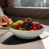 White bowl with various fruits like apples, grapes, and strawberries on a table