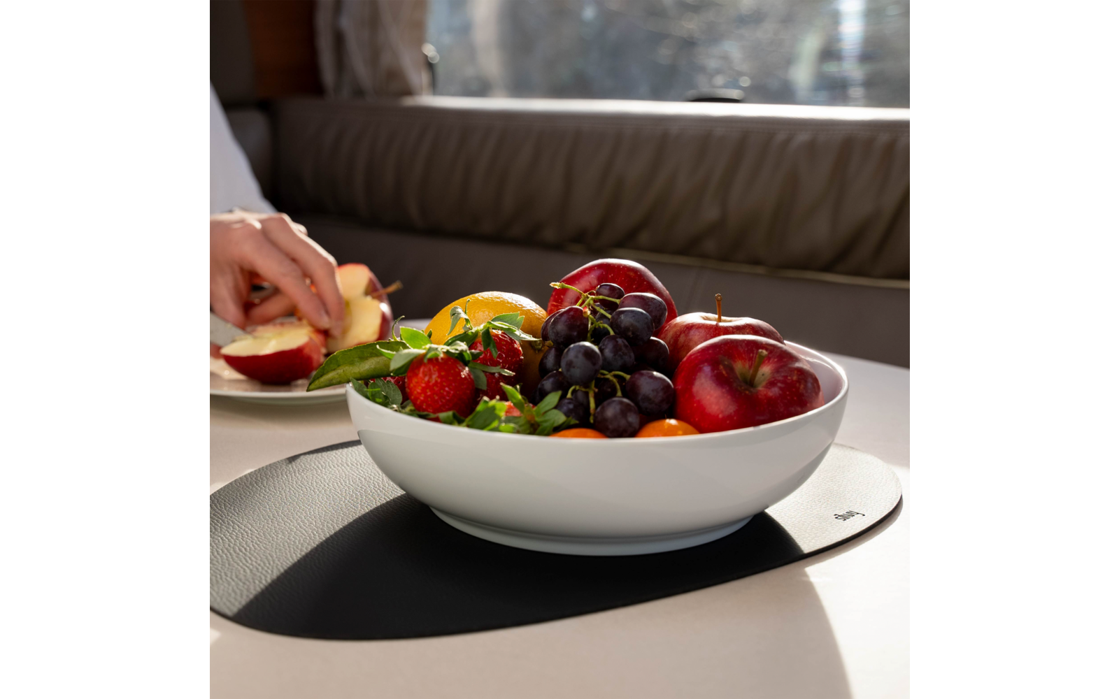 White bowl with various fruits like apples, grapes, and strawberries on a table