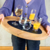 Person holding a round wooden tray with two glasses of orange juice, two glasses of water, and one wine glass with a drink