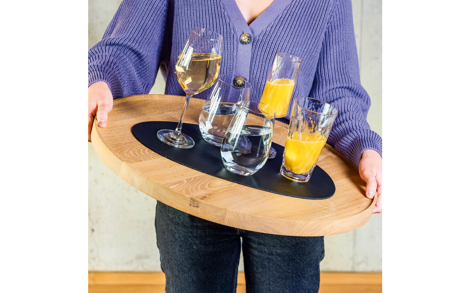 Person holding a round wooden tray with two glasses of orange juice, two glasses of water, and one wine glass with a drink