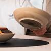 A hand holds an upside-down beige and black bowl above a table