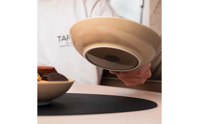 A hand holds an upside-down beige and black bowl above a table