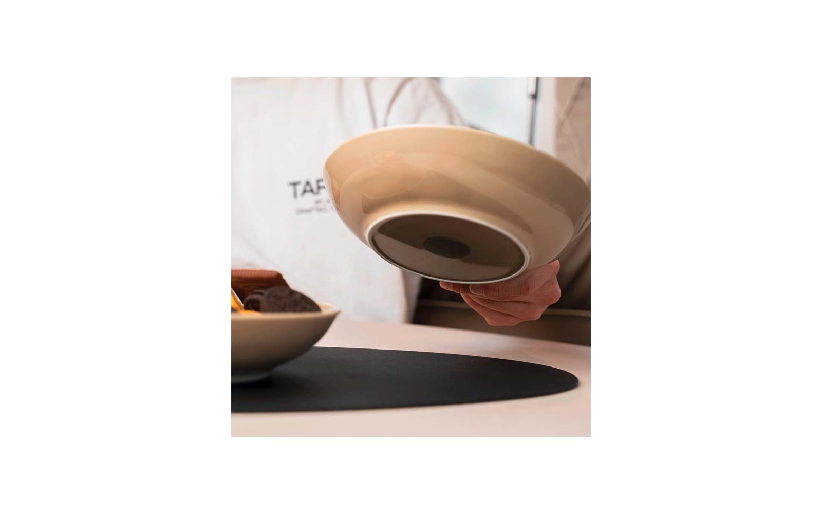 A hand holds an upside-down beige and black bowl above a table
