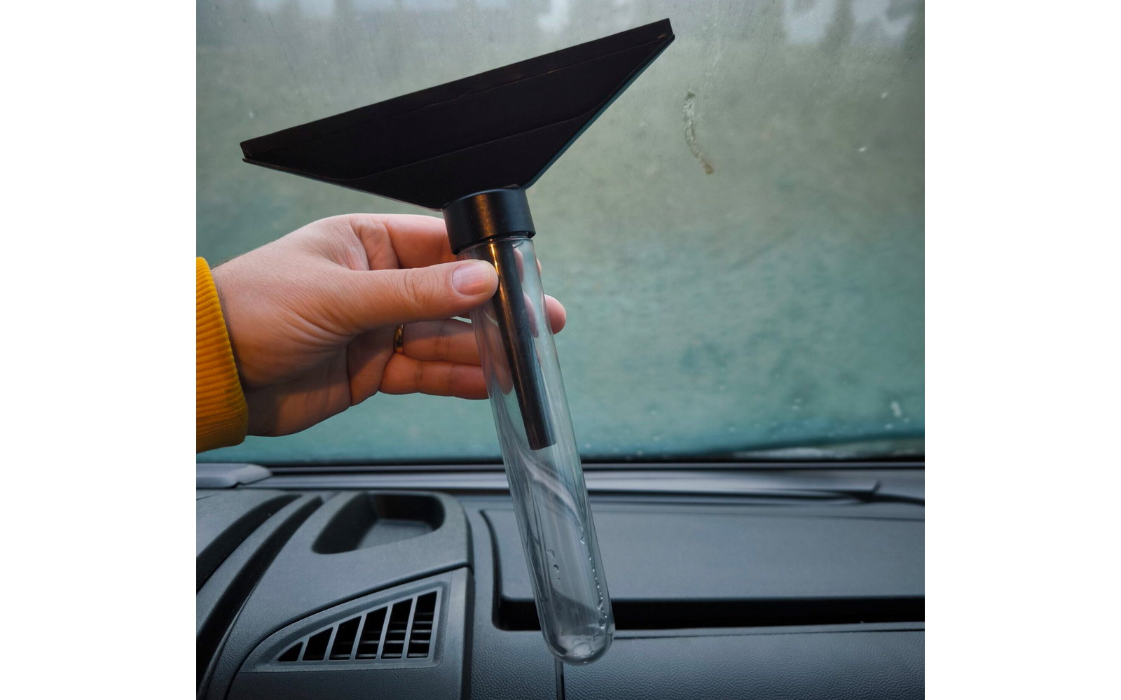 Hand hält ein Messgerät mit Trichter über einem Autoarmaturenbrett