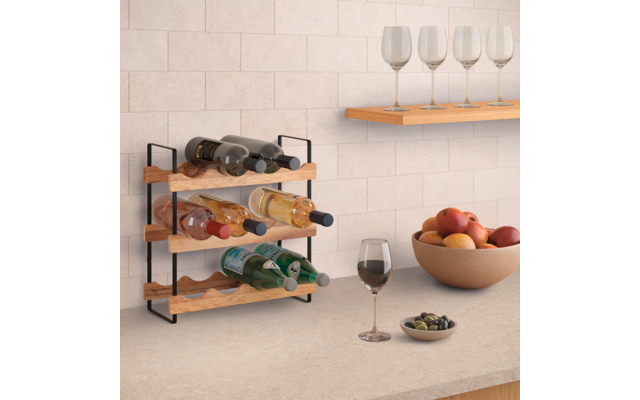 Kleines Holz-Weinregal mit schwarzem Metallgestell und sechs Weinflaschen auf einer Küchenarbeitsplatte; darüber an der Wand ein Regal mit vier leeren Weingläsern. Auf der Arbeitsplatte ein gefülltes Weinglas, eine Schale mit Obst und eine kleine Sch