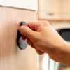 Hand dreht schwarzen Drehknopf an hellem Holzschrank