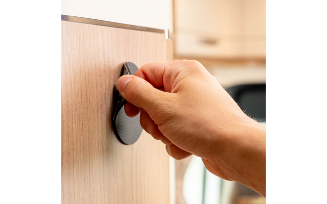 Hand dreht schwarzen Drehknopf an hellem Holzschrank