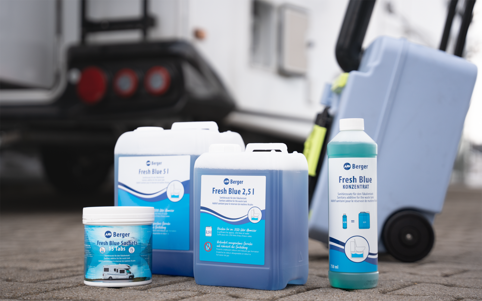 Mehrere blaue Kunststoffbehälter mit Etiketten (Dose, Flaschen, Kanister) auf Asphalt neben einer Sackkarre und dem Heck eines Fahrzeugs