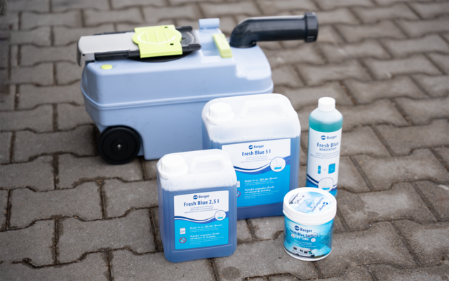 Hellblaues Gerät mit schwarzem Griff und zwei Rädern auf gepflastertem, gepflastertem Boden; davor vier Kunststoffbehälter mit blauen Etiketten: zwei Kanister, eine Flasche und ein runder Behälter