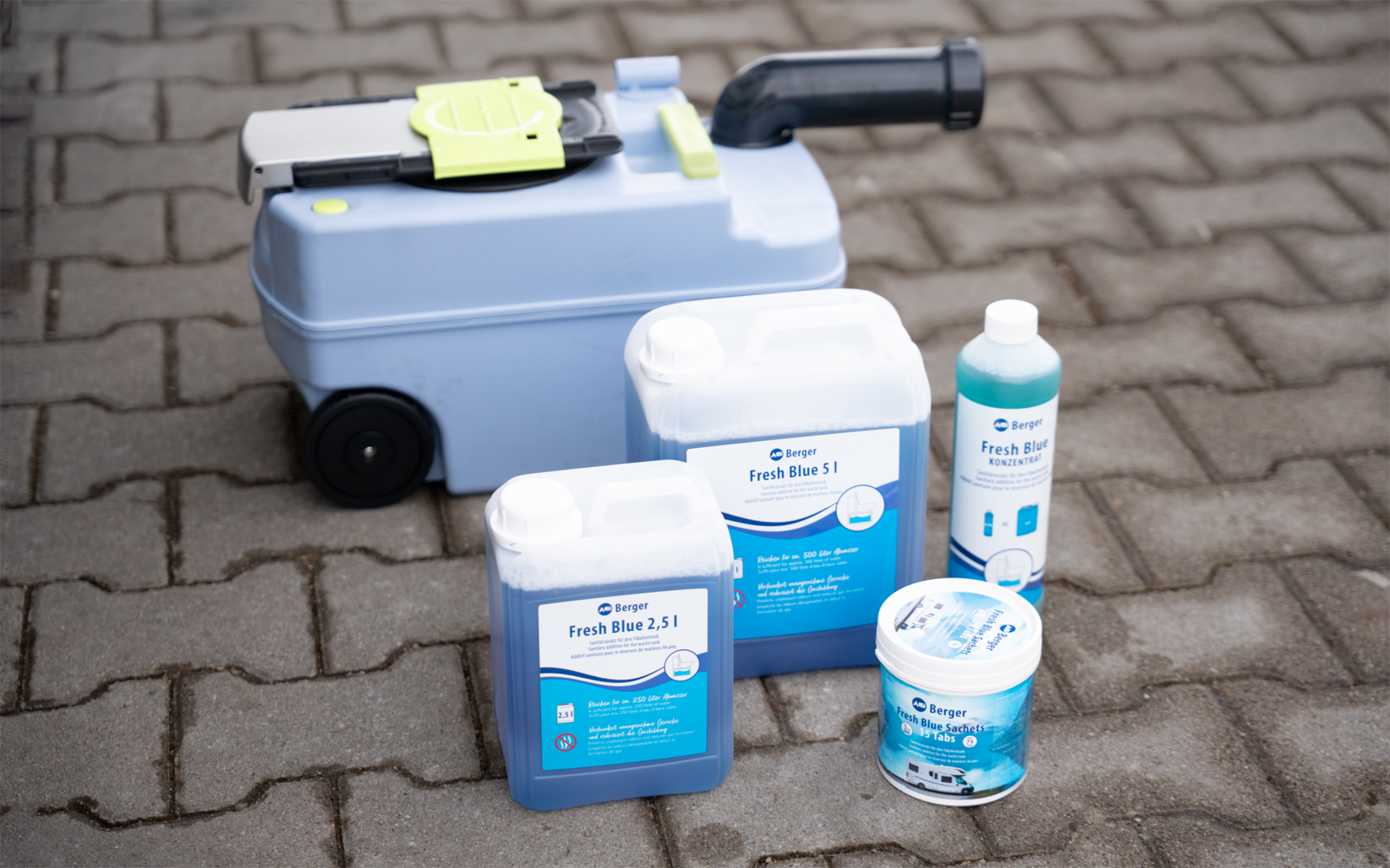 Hellblaues Gerät mit schwarzem Griff und zwei Rädern auf gepflastertem, gepflastertem Boden; davor vier Kunststoffbehälter mit blauen Etiketten: zwei Kanister, eine Flasche und ein runder Behälter