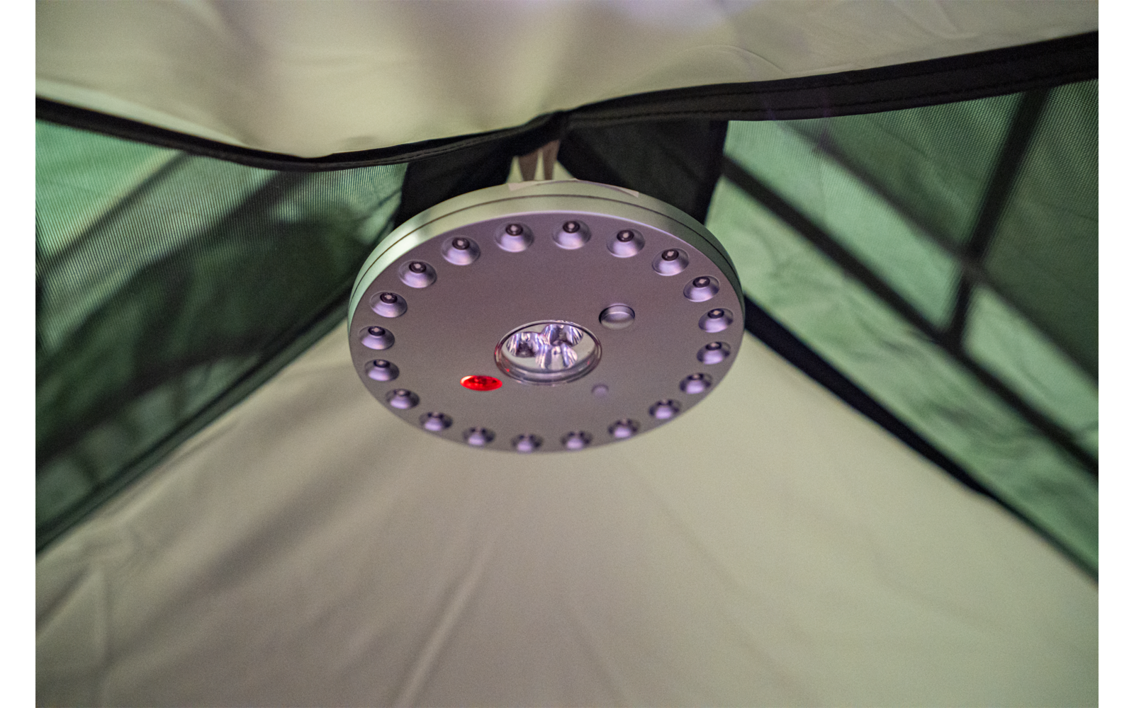 Runde LED-Lampe mit zentraler Linse und rotem Punkt an einer Zeltdecke