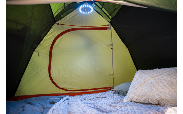 Innenraum eines Zeltes mit gelber Innenwand und rotem Reißverschluss, rundes LED-Licht an der Dachspitze, blaues Bettzeug, gemusterte Decke und flauschiges Kissen