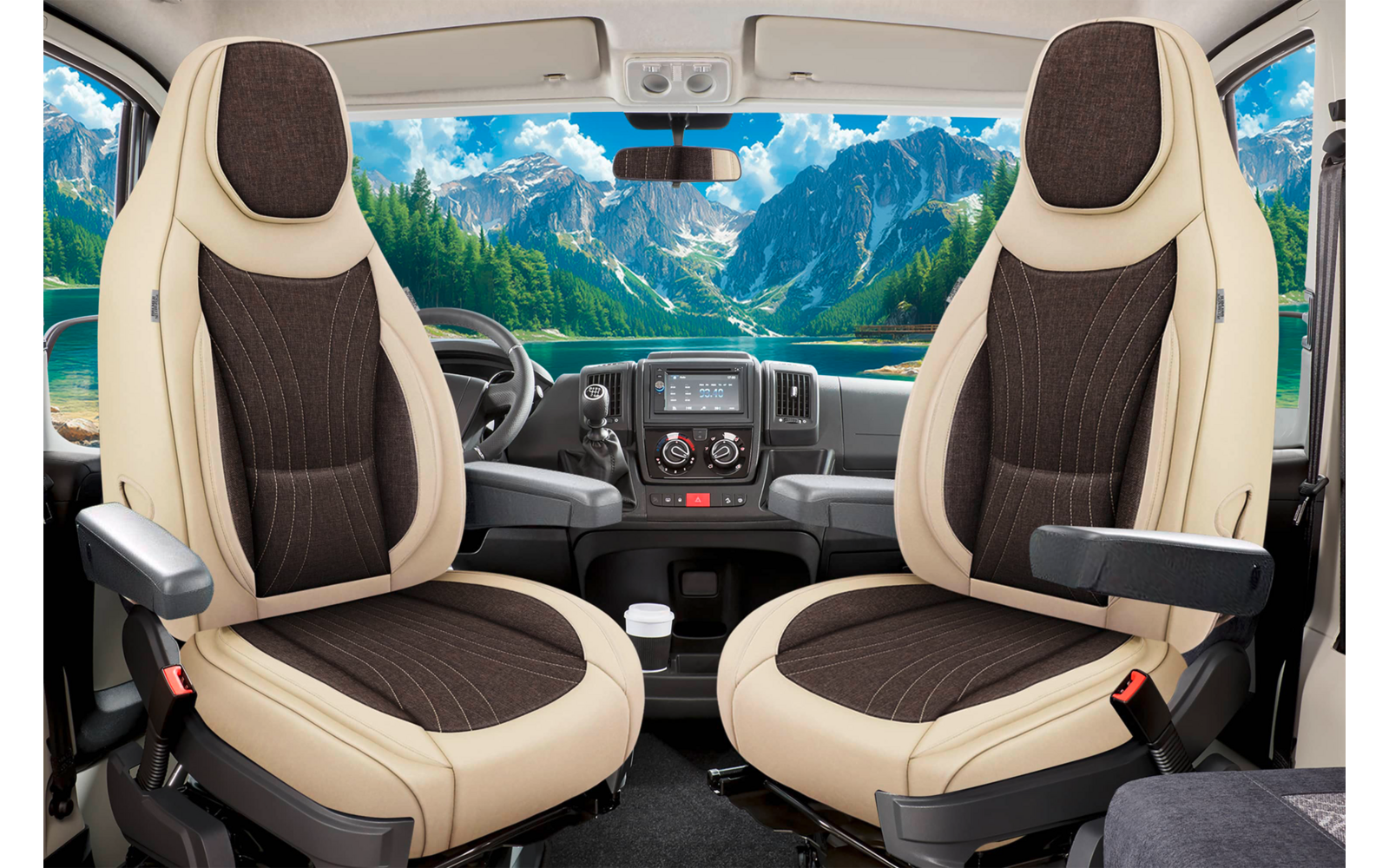 Blick auf zwei gedrehte beige-braune Vordersitze und das Armaturenbrett eines Fahrzeugs; durch die große Frontscheibe sichtbar: Berglandschaft mit See, Bäumen und blauem Himmel