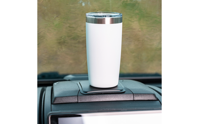 Witte beker met doorzichtig deksel en zilveren rand in een bekerhouder op het dashboard van een auto, vervaagde buitenaanzicht door de voorruit